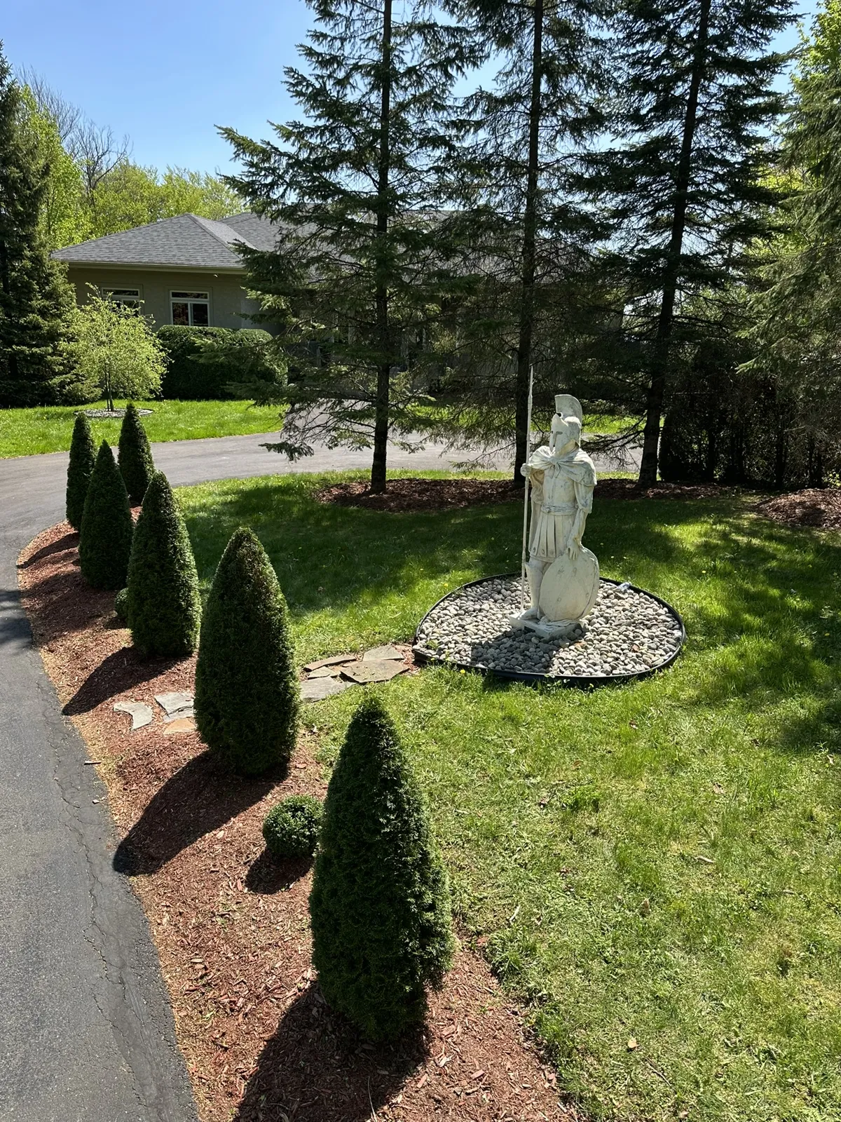 Entrée aménagée sur mesure : statue de guerrier spartiate sur lit de galets, cèdres taillés en cône alignés le long de l’allée
